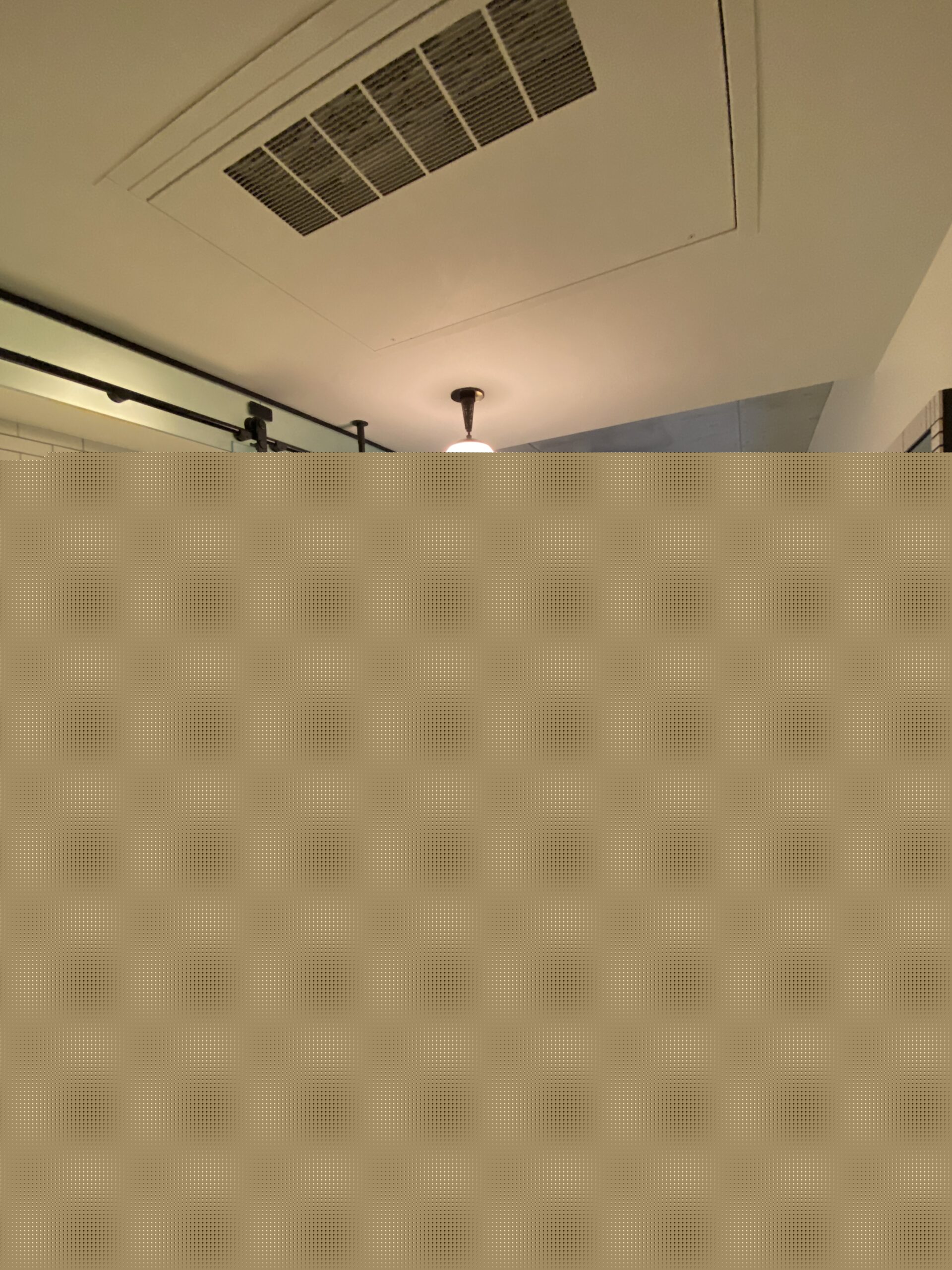 Compact hotel room with an open tiled shower, black vanity, and a bed at the far wall.