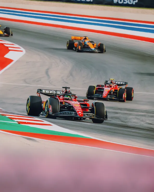 Two red Ferrari Formula 1 cars lead an orange McLaren past red-white-and-blue runoff at Circuit of the Americas.