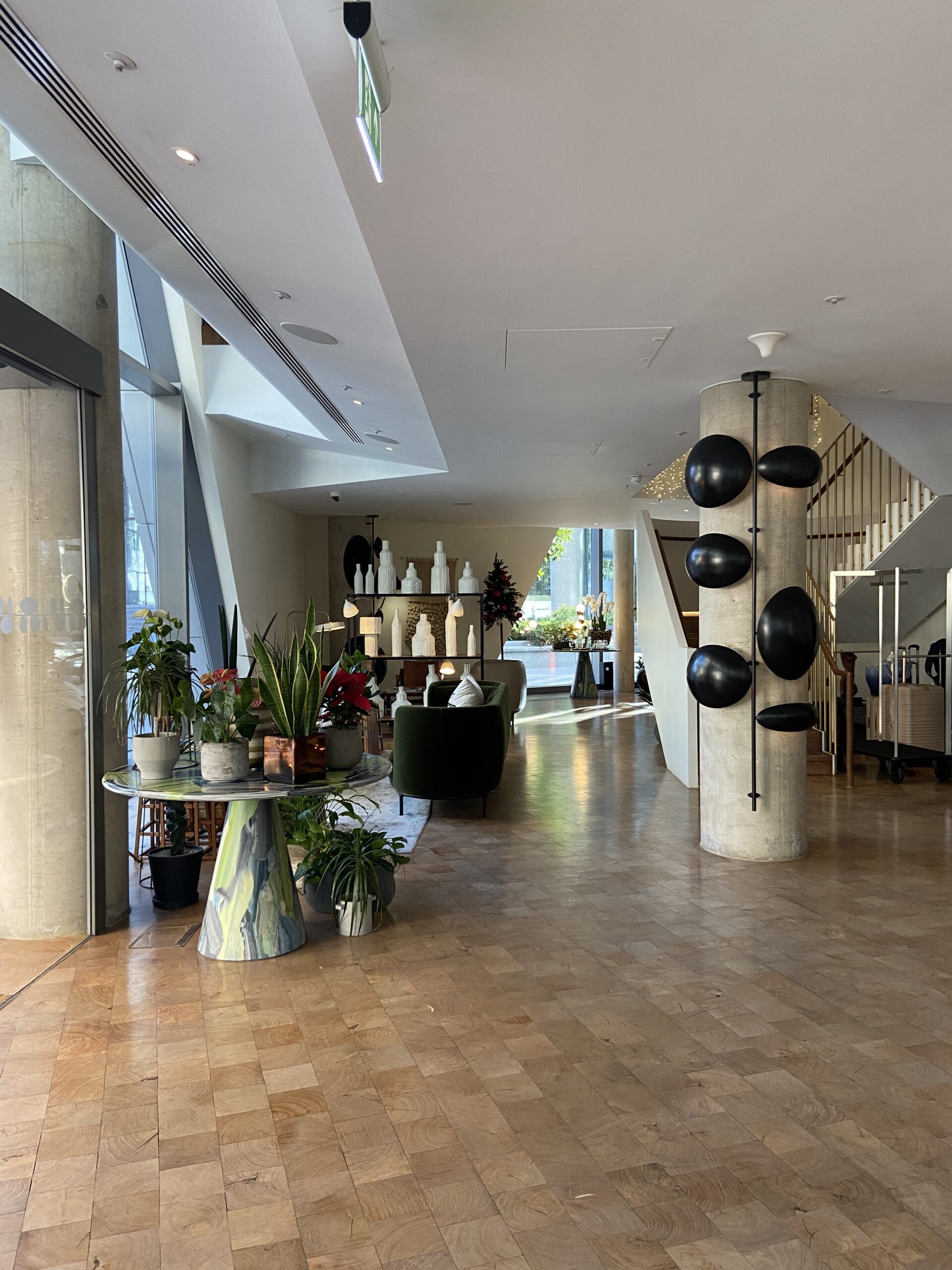 Bright lobby with a marble plant table, a concrete column holding black pebble sculptures, and a green armchair.