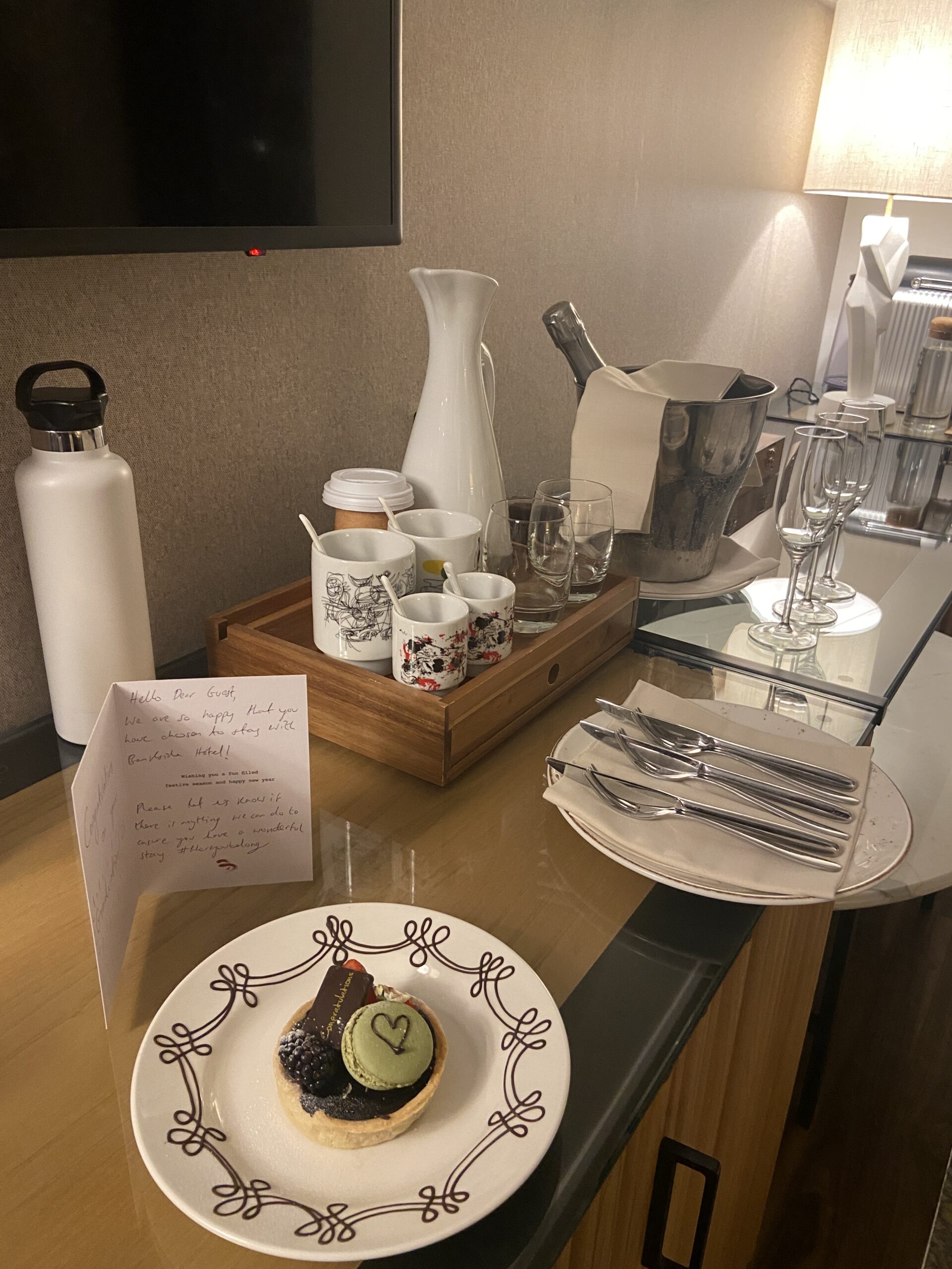 Bankside Hotel welcome tart and note beside a tea tray, plates, and a cloth-wrapped bottle in an ice bucket.