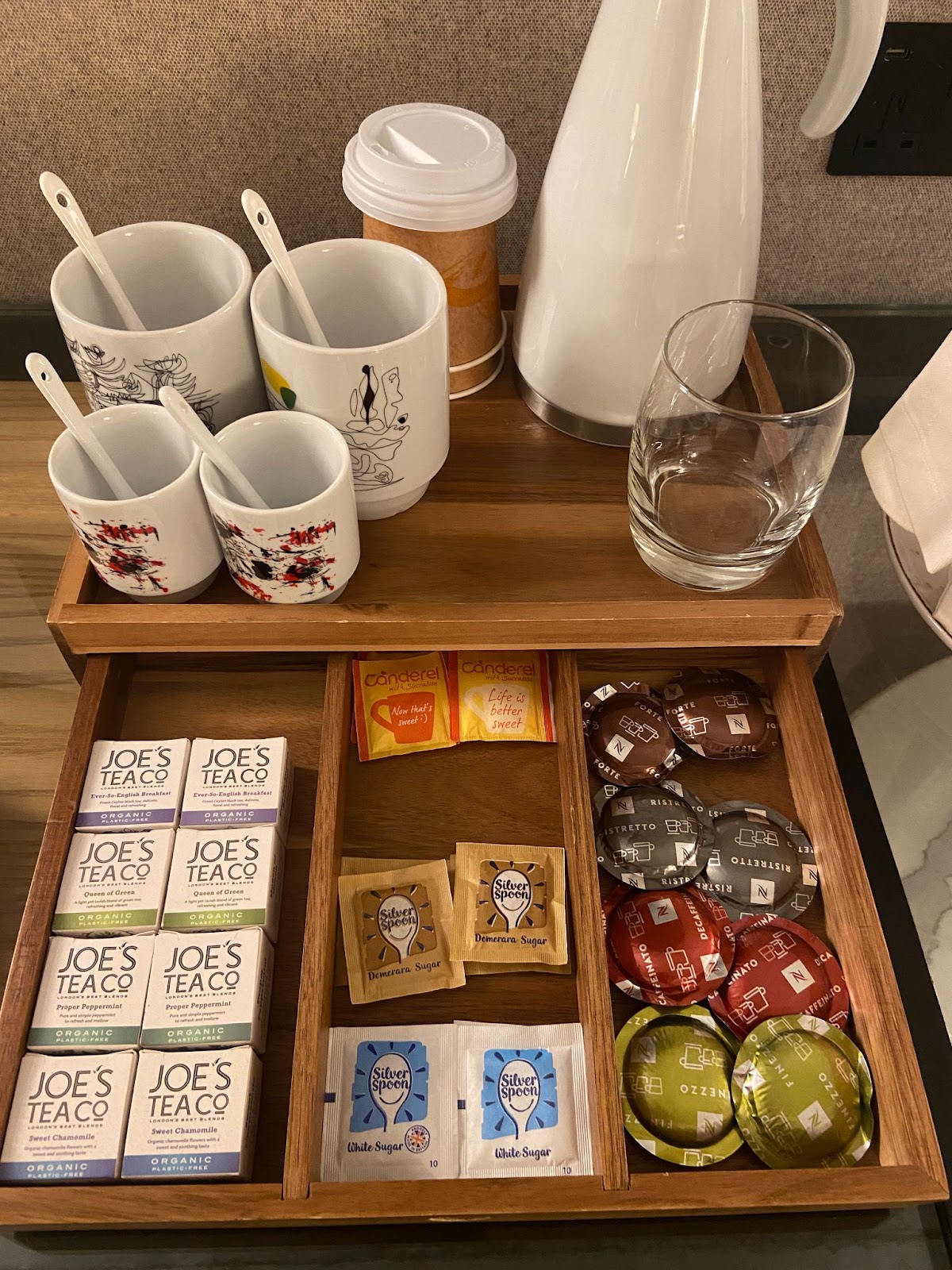 Hotel tea tray with a white kettle, illustrated mugs, Joe's Tea packets, and coffee capsules in the drawer.