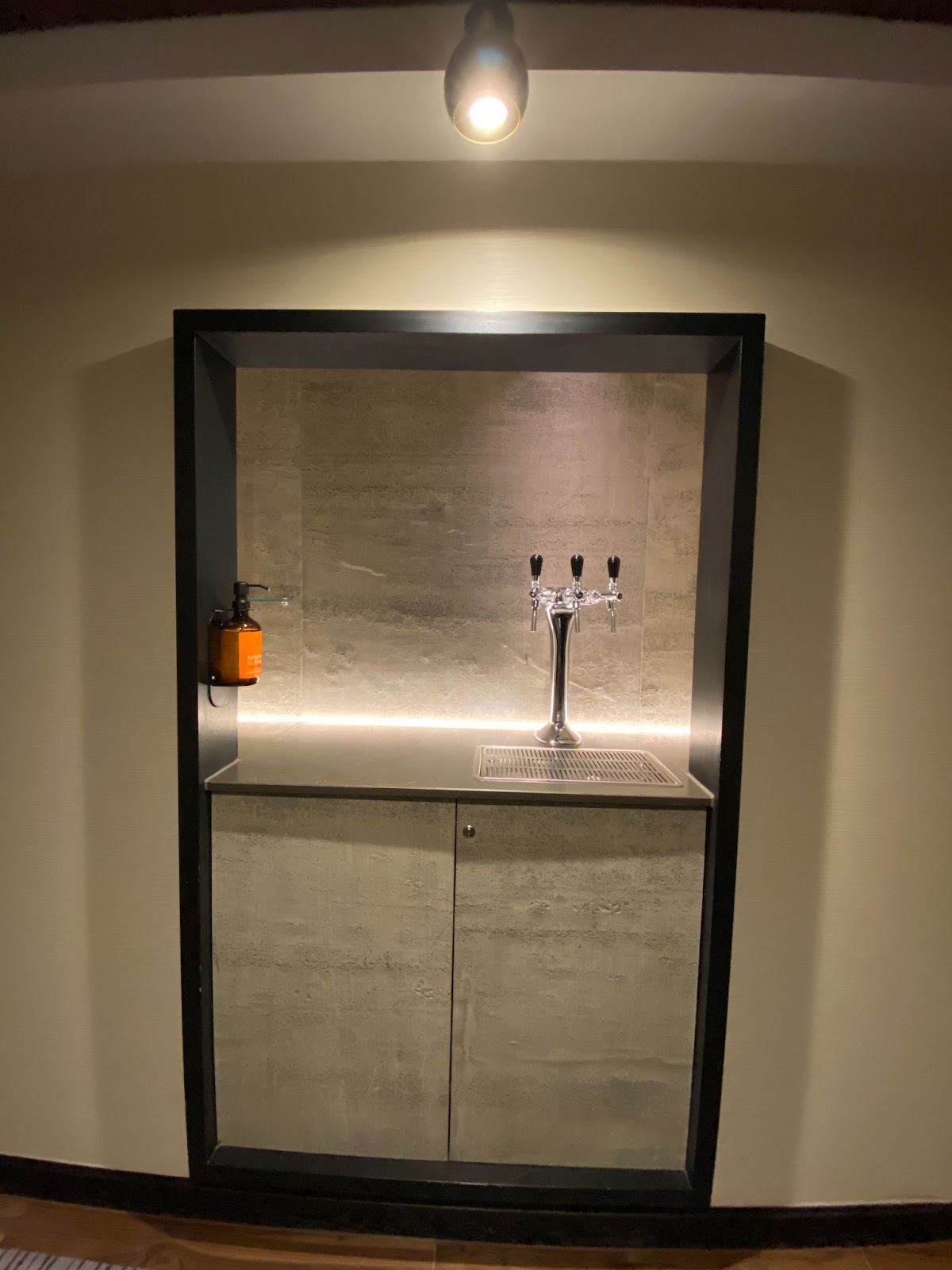 Recessed stone alcove with a three-tap chrome draft tower and a single orange pump bottle.