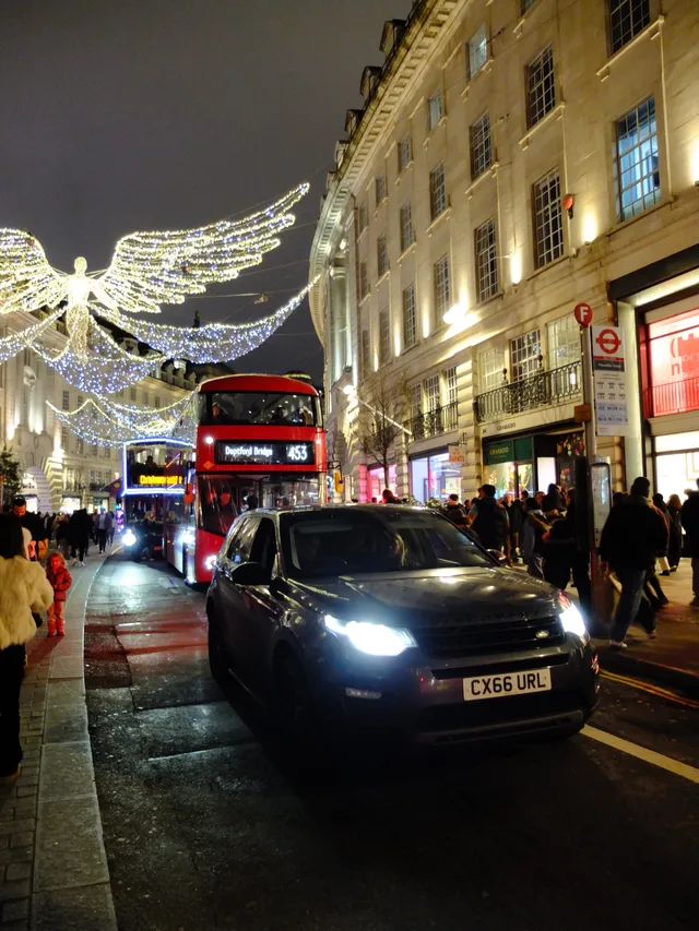 Night on a London shopping street with Christmas angel lights over a red double-decker bus.