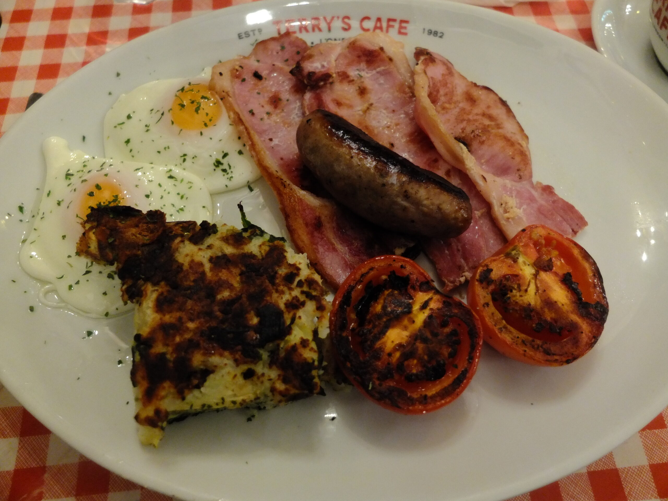 Terry's Cafe breakfast of fried eggs, bacon, sausage, grilled tomatoes, and a fried potato cake.