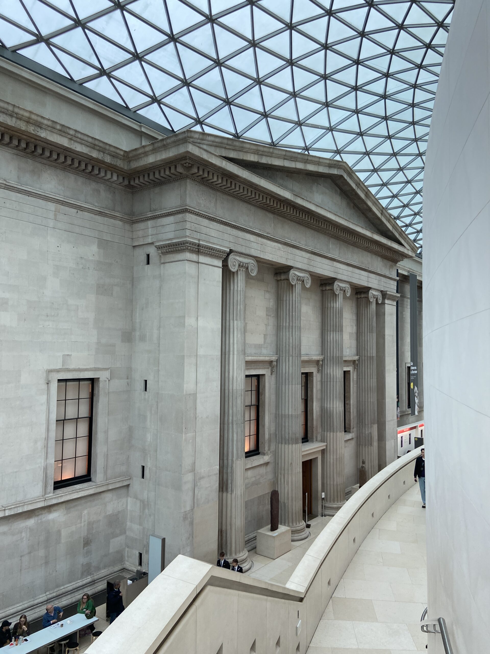 Ionic stone colonnade under a curved glass-and-steel lattice roof, with a white ramp in the foreground.
