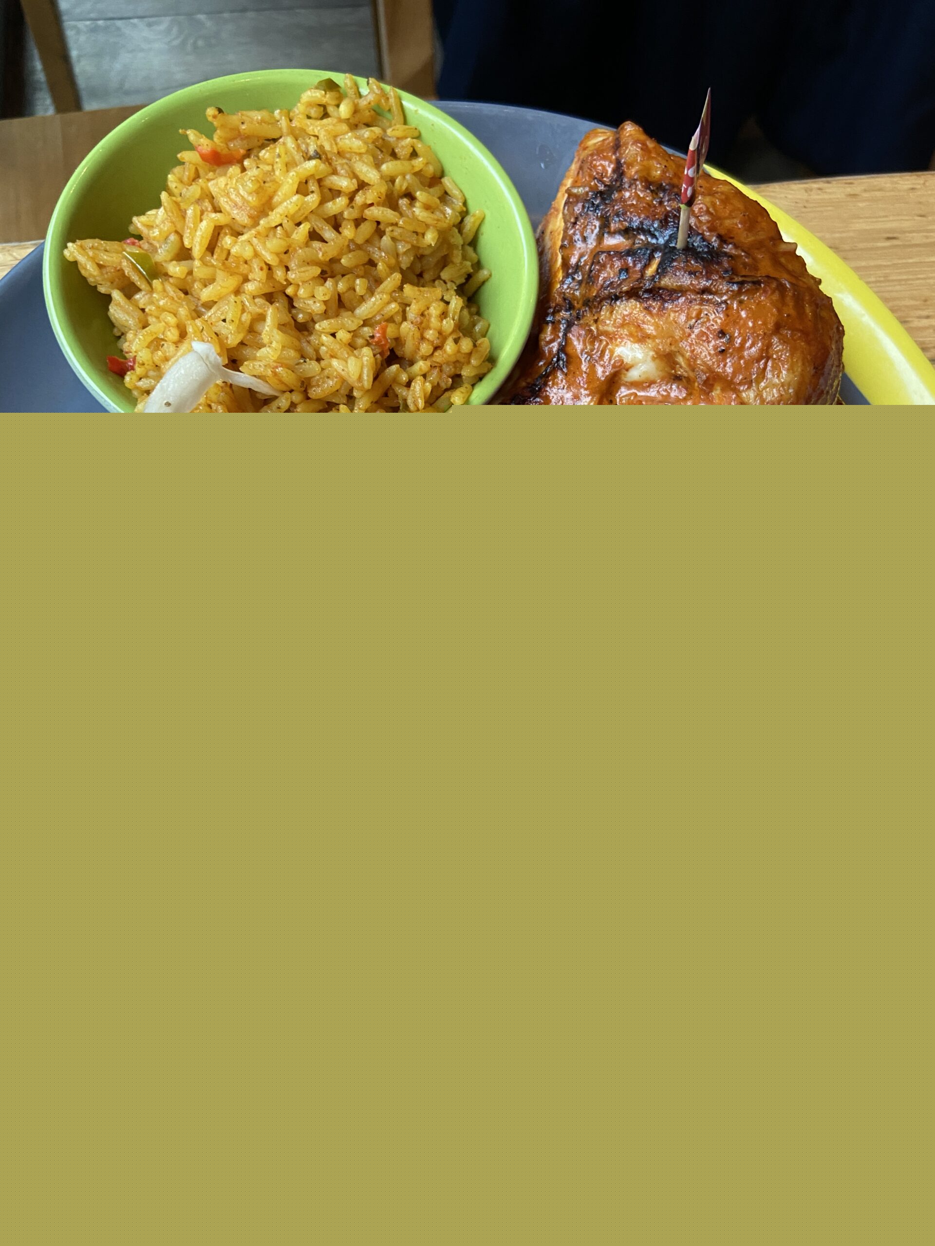 Half a charred peri-peri chicken on a dark plate with yellow rice and coleslaw in small bowls.