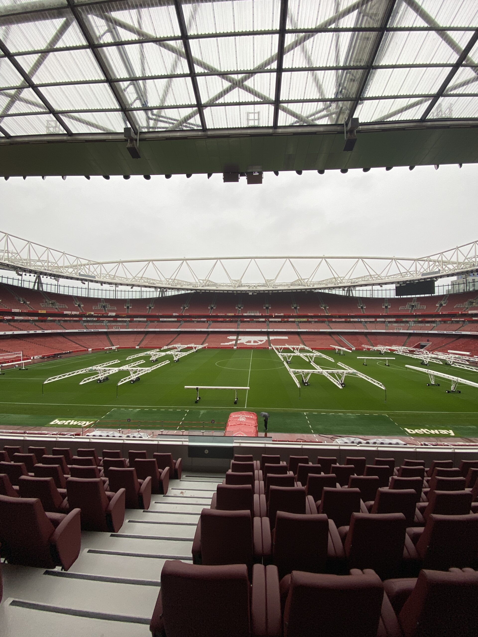 Empty Emirates Stadium from the upper red seats, with turf lights on the pitch and the white cannon in the far stand.