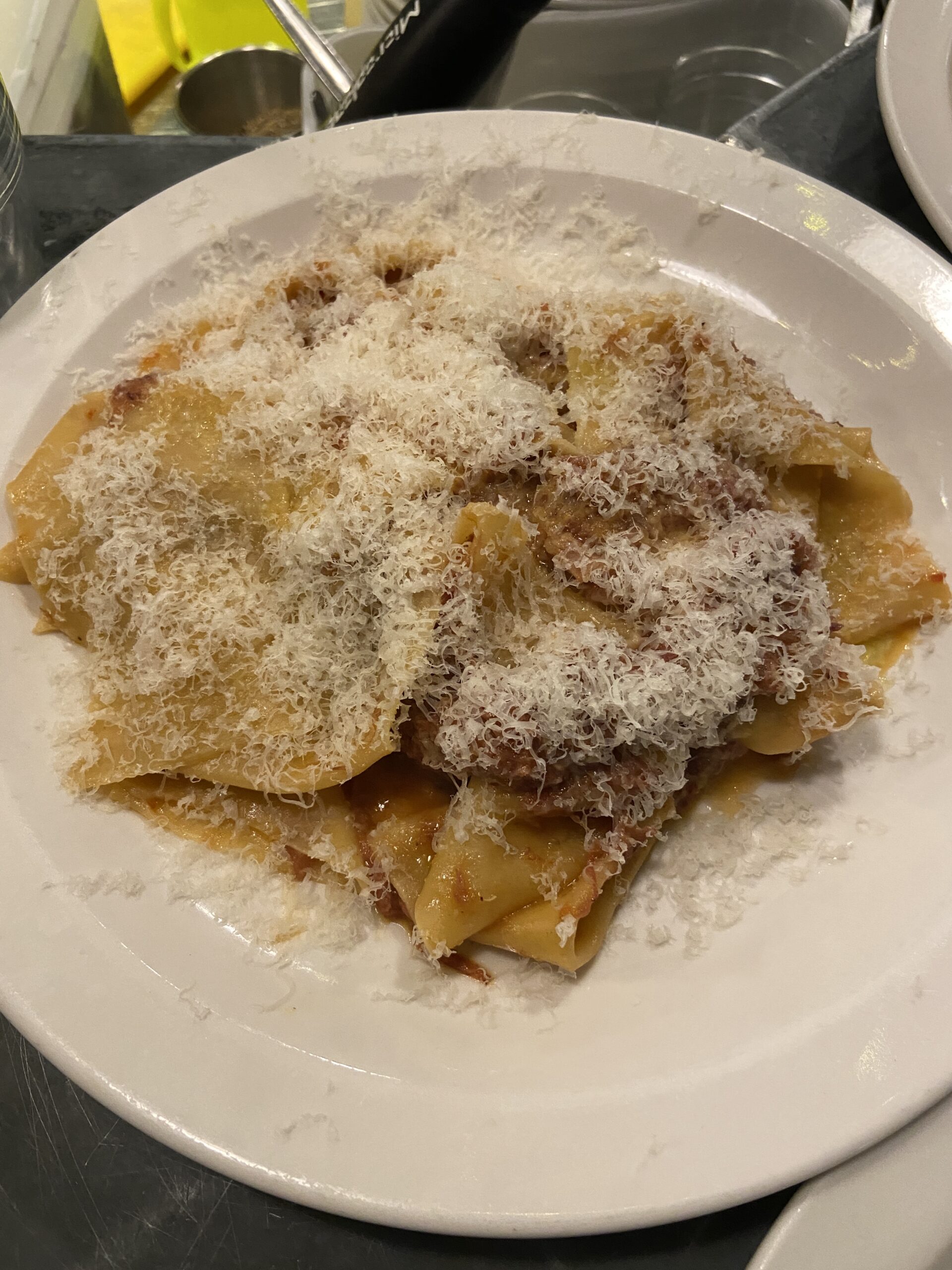 Wide pasta ribbons in a meat ragu, buried under a thick layer of grated white cheese.