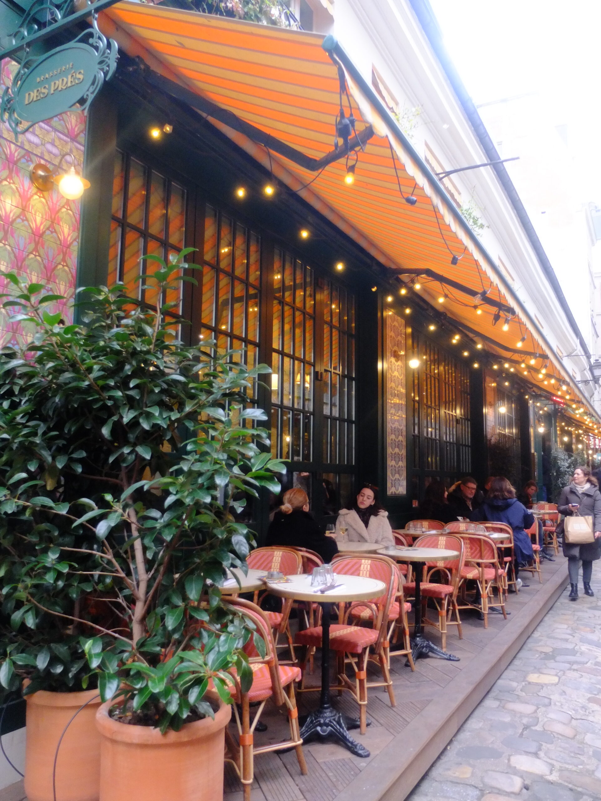 Outdoor tables under an orange-and-white striped awning at Brasserie Des Prés.