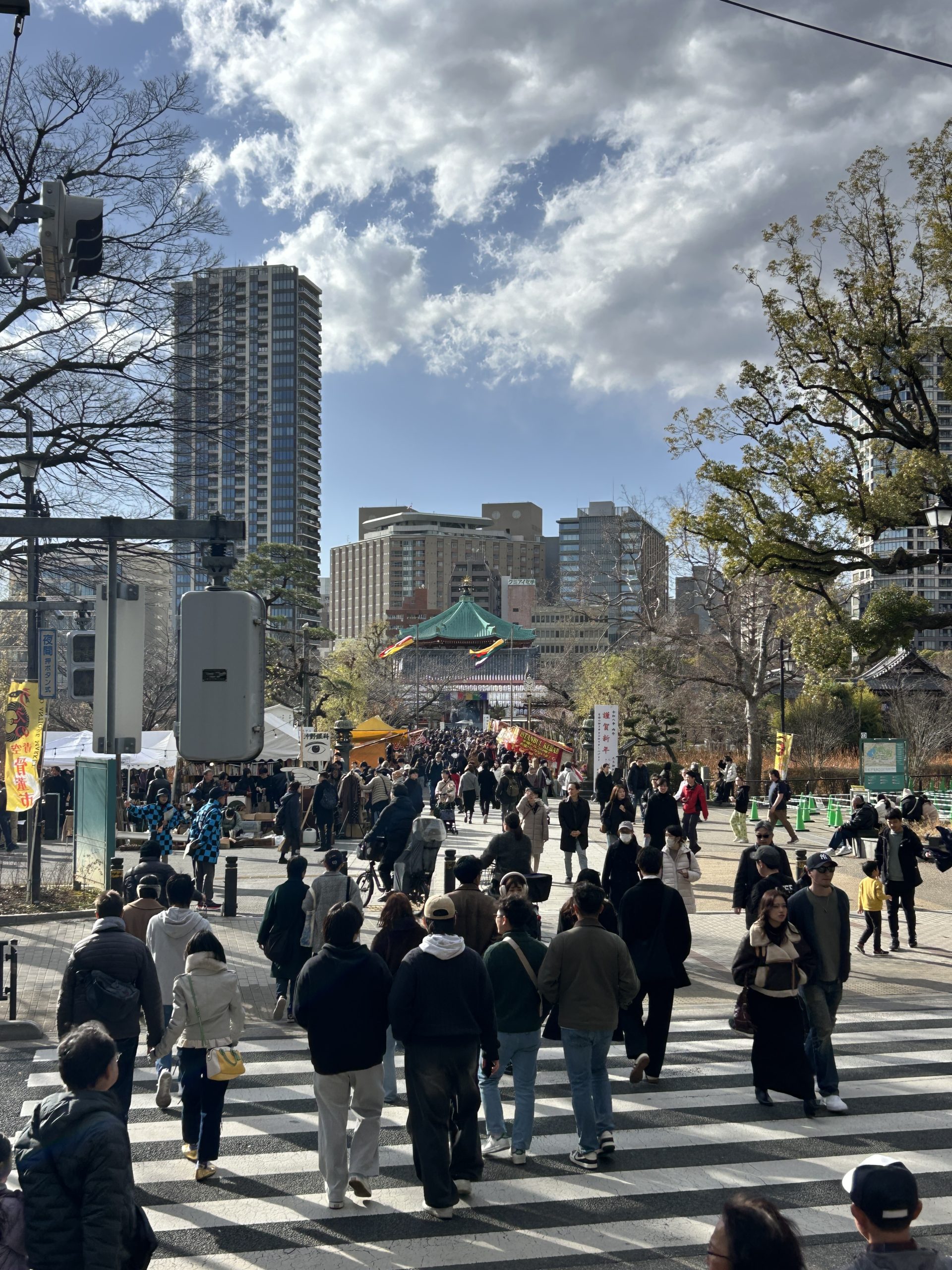 Crowd crossing toward a green-roofed temple, with market tents and skyscrapers behind.
