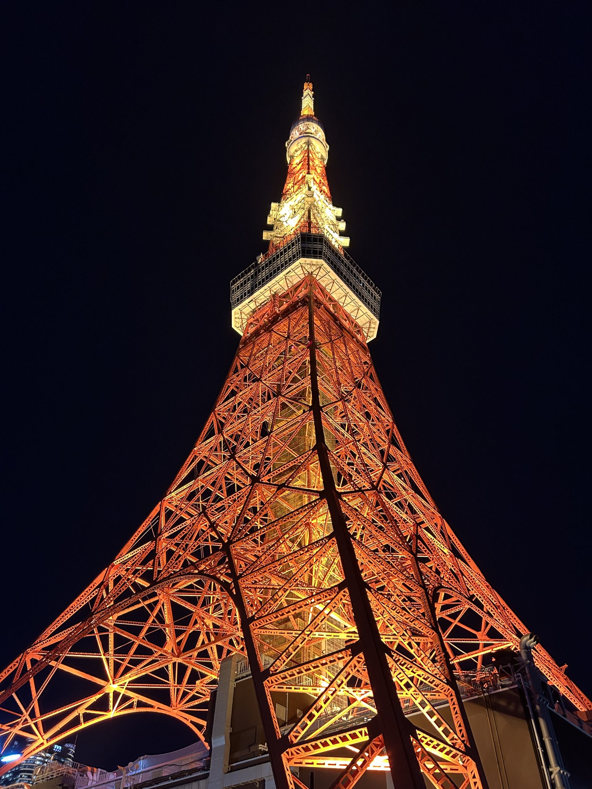 Low-angle night view up the orange-lit lattice of Tokyo Tower to the white observation deck.